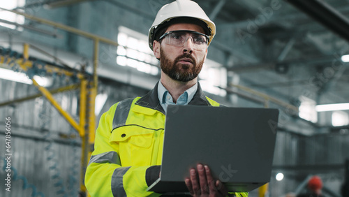 European worker wearing yellow vest, hardhat and safety glasses holds laptop and write something down. Manager looks at gadget screen, takes notes or searches for information on Internet.