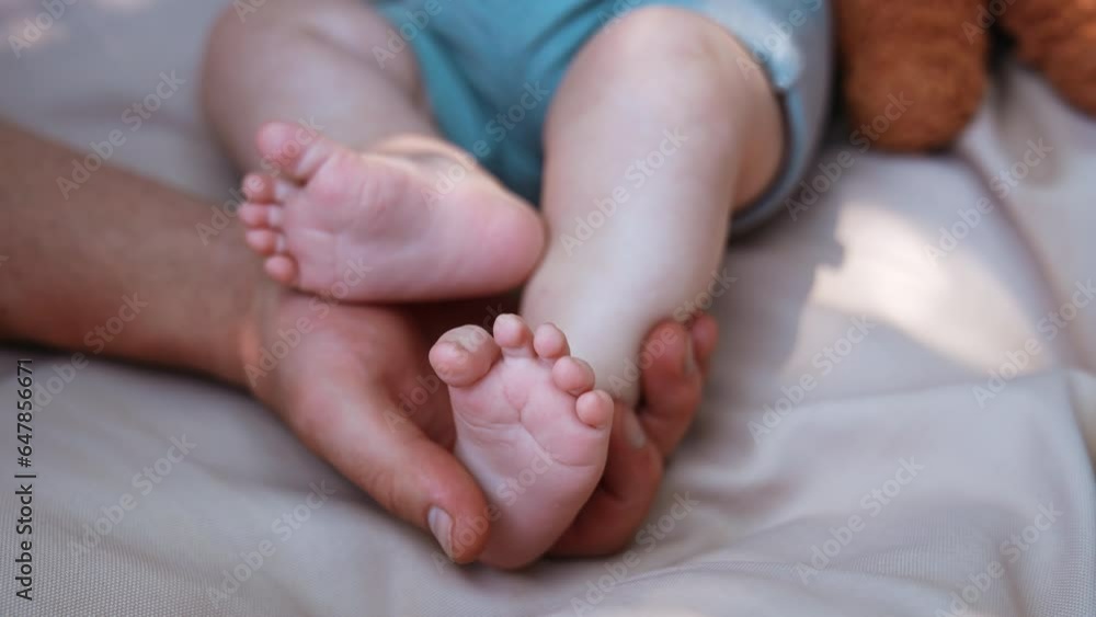 Dad's hand holding tenderly a tiny baby foot. Infant tossing his feet as father touches them. Close up. Dad's hand holding tenderly a tiny baby foot. Infant tossing his feet as father touches them. Close up.