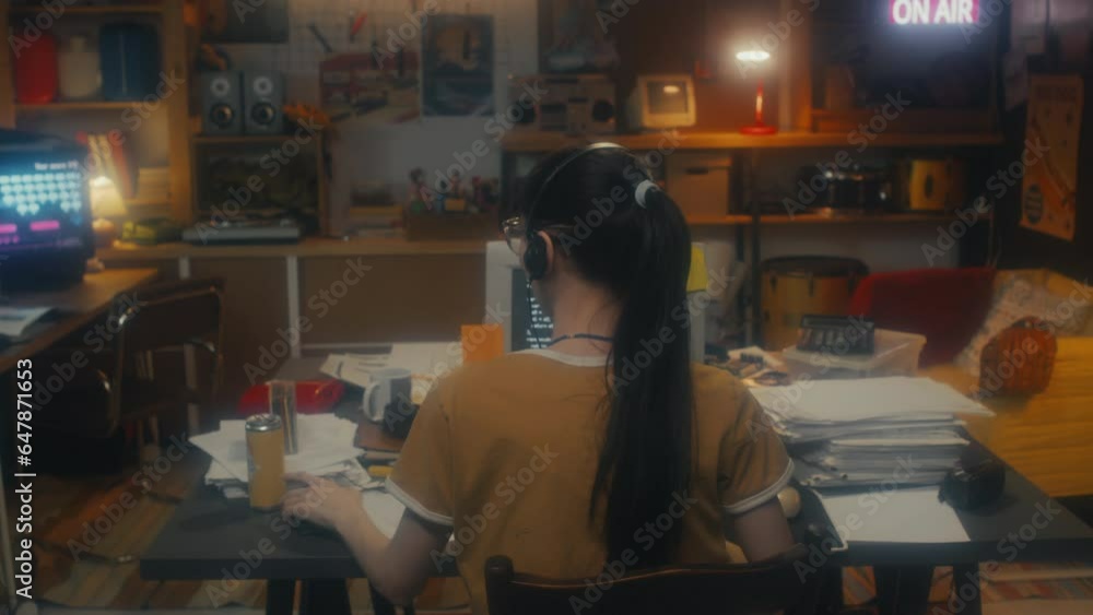 Rear view of unrecognizable young female IT specialist with ponytail hairstyle putting on headphones and turning on personal stereo to listen to music at work Rear view of unrecognizable young female IT specialist with ponytail hairstyle putting on headphones and turning on personal stereo to listen to music at work