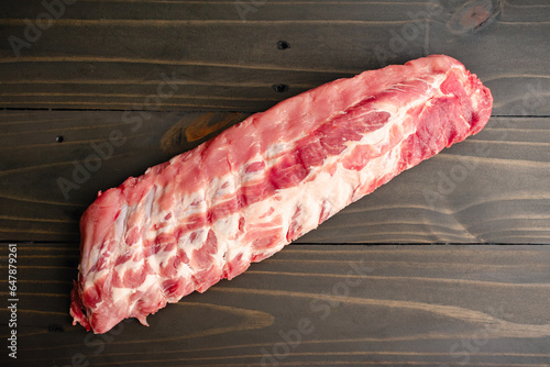 Raw Rack of Baby Back Ribs on a Wooden Table: An uncooked rack of pork loin ribs viewed from directly above