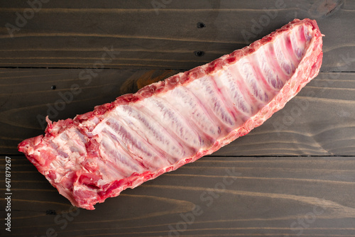 Raw Rack of Baby Back Ribs Underside on a Wooden Table: An uncooked rack of pork loin ribs viewed from directly above