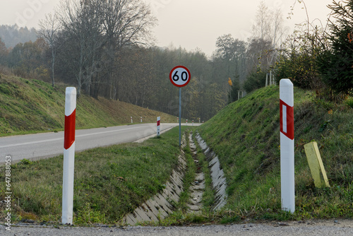 Droga, biało-czerwone słupki, znak ograniczenia prędkości.