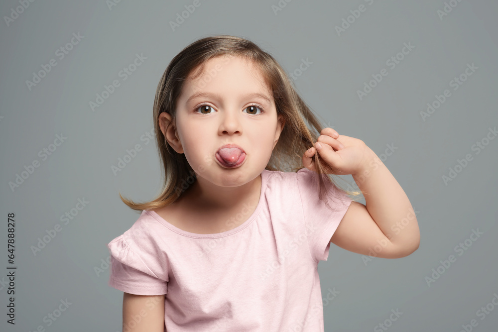 Funny little girl showing her tongue on grey background Funny little girl showing her tongue on grey background