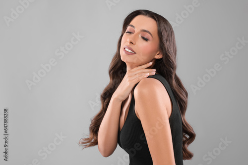 Hair styling. Beautiful woman with wavy long hair on grey background