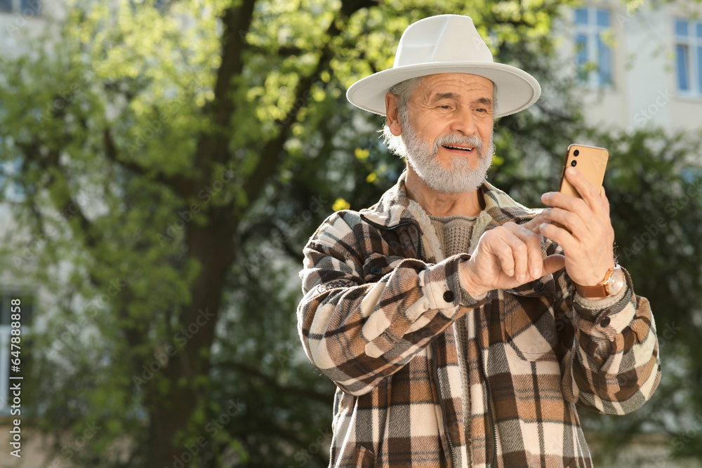 Handsome senior man using smartphone outdoors, space for text Handsome senior man using smartphone outdoors, space for text