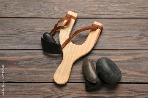 Slingshot with stones on wooden background, flat lay
