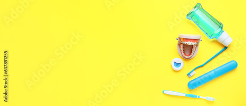 Model of jaw with dental braces, mouth rinse, floss and toothbrushes on yellow background with space for text