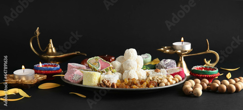 Plate with Indian treats and lamps on dark background. Divaly celebration
