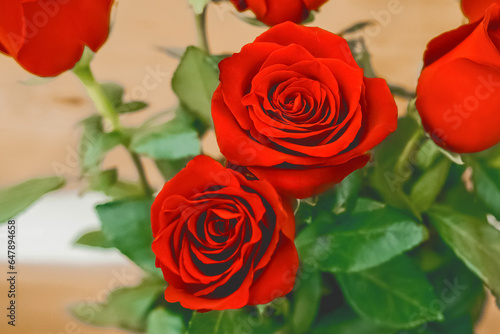 Bouquet of red rose flowers with green leaves on a wooden background  close up