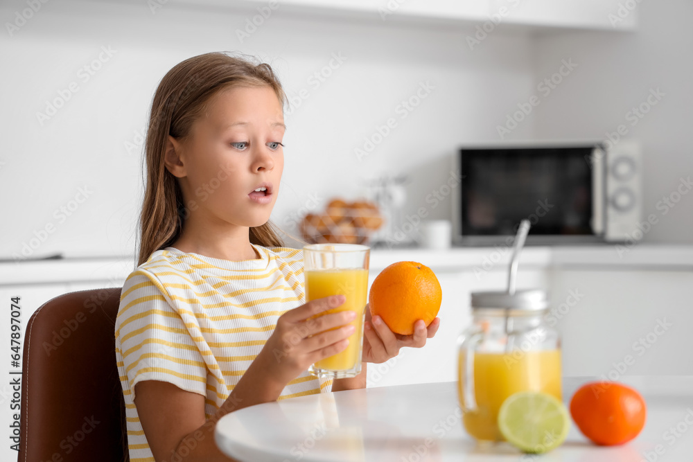 Little girl with glass of fresh citrus juice sitting at table in kitchen Little girl with glass of fresh citrus juice sitting at table in kitchen