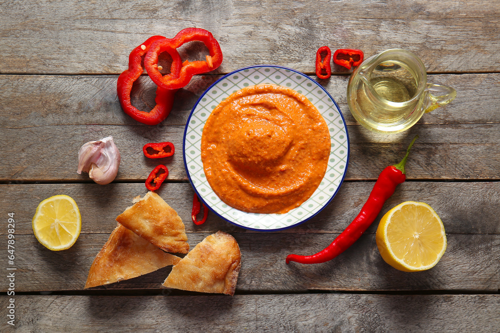 Fototapeta premium Plate of tasty muhammara and ingredients on wooden background