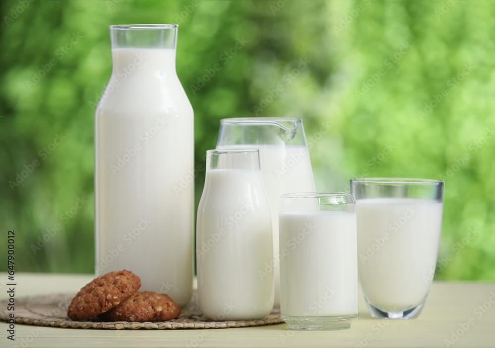 Glasses and bottles of fresh milk with sweet cookies on yellow wooden table outdoors Glasses and bottles of fresh milk with sweet cookies on yellow wooden table outdoors