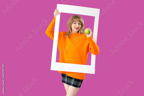 Young woman with apple and frame on purple background