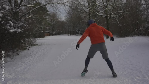 Wrong outfit and footwear for running on slippery surfaces in winter. Man jogging in snow cold weather and slips. Slippery sneakers with wrong soles for trail running on ice covered paths in woods.  photo