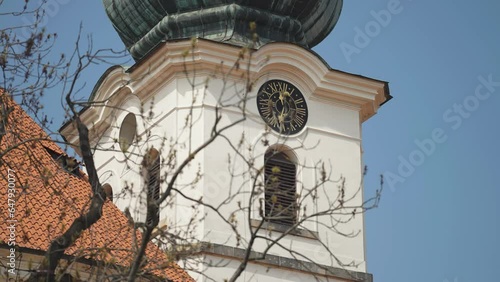 A tower with a clock. Roof tiles and leafless tree branches in the foreground. Slow-motion parallax shot. photo