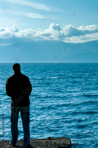 Figura di ragazzo che pesca in silhouette di fronte il mare dello Stretto photo