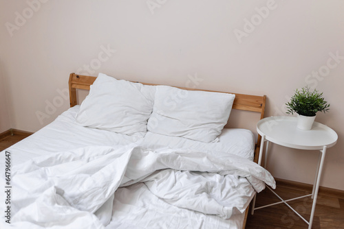 Unmade bed with white messy crumpled blanket, pillows and sheet. Mess in bedroom, cheap hotel or appartment room