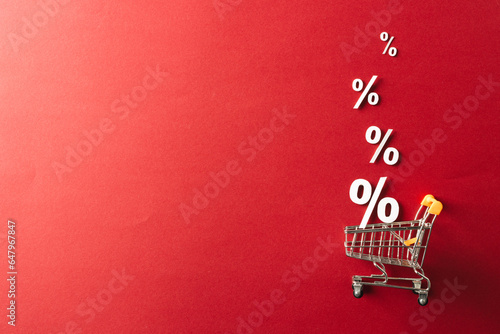 Shopping trolley and white percent signs with copy space on red background photo