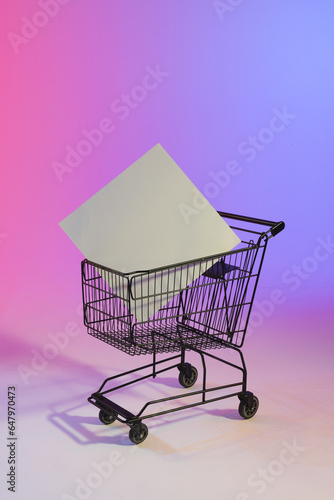 Vertical image of shopping trolley with blank canvas and copy space over neon purple background