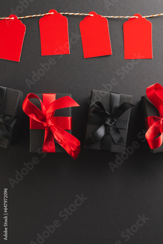 Vertical image of red gift tags on pegs and black gift boxes with copy space over black background