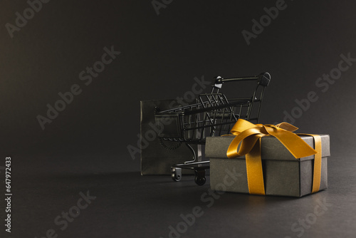 Gift box with ribbon, gift bag and shopping trolley with copy space over black background
