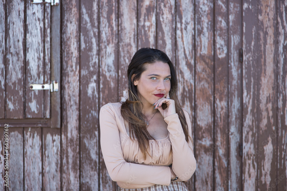Attractive young woman, with blue eyes, sweater and plaid skirt, with her hand on her chin in a pensive attitude, on a wall of wooden planks. Concept thoughts, expressions. Attractive young woman, with blue eyes, sweater and plaid skirt, with her hand on her chin in a pensive attitude, on a wall of wooden planks. Concept thoughts, expressions.