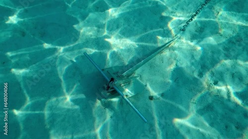 Danforth anchor secured in a sand bottom with light shining through tropical blue water