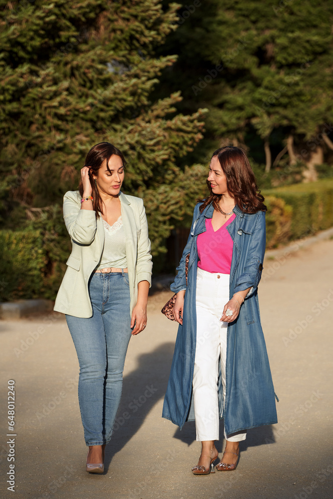 Two stylish female friends talking while walking together outdoors. Friendship concept.