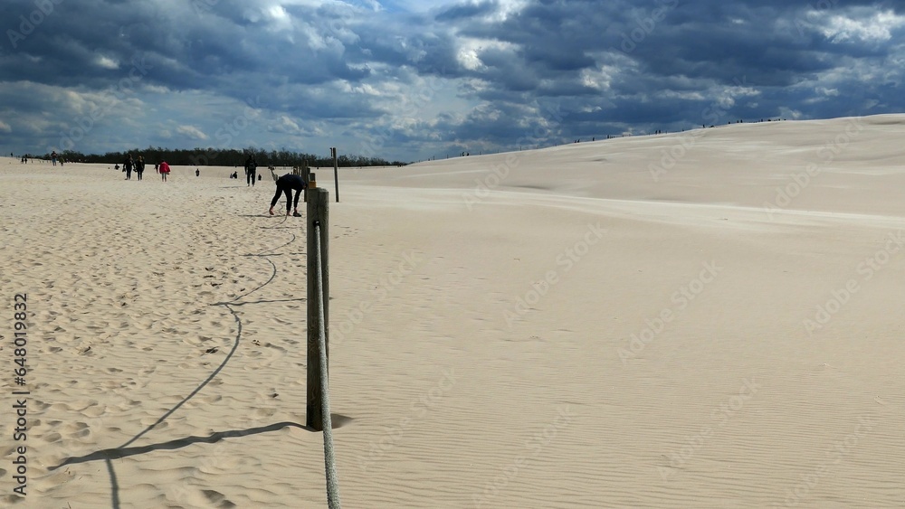 Tourists on Sandy Desert and Dark Storm Clouds