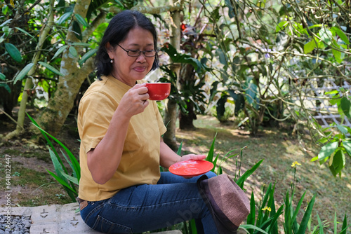 Asian woman sitting in the garden alone drinking her morning tea photo