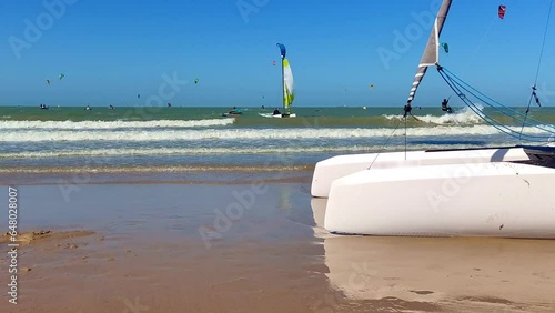 Sailingboat resting on a beach on a sunny summerday with surfers and sailingboats in the background at sea photo
