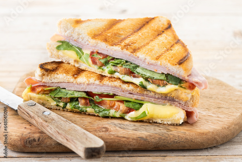 Panini sandwich with ham, cheese, tomato and arugula on wooden table