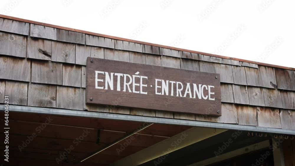 A Rustic Wooden White Painted Entrance Entrée Sign Against a Shingled Roof on a Local Canadian Outdoor Farmers Market Business A Rustic Wooden White Painted Entrance Entrée Sign Against a Shingled Roof on a Local Canadian Outdoor Farmers Market Business
