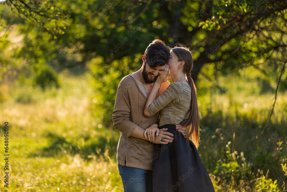 girl says something in the ear of her boyfriend, walking in nature girl says something in the ear of her boyfriend, walking in nature