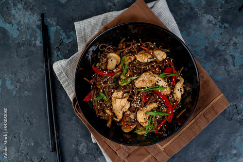 Asian wok noodles with chicken and vegetables with chopsticks on the table.