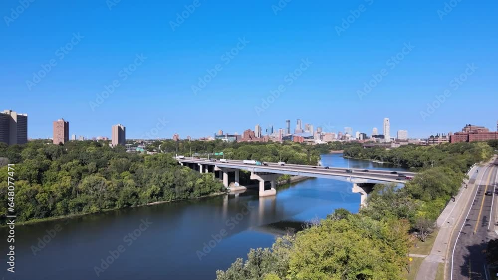 Reveal through the green trees the Minneapolis skyline in the summer just over the river and the hiawatha highway and bridges Reveal through the green trees the Minneapolis skyline in the summer just over the river and the hiawatha highway and bridges