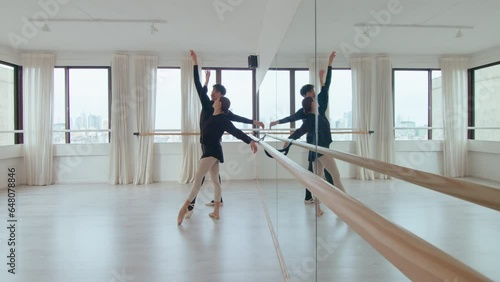 Young ballet couple performing slow synchronic moves with graceful arms and turn in a spacious dance studio with mirror wall. Full shot, copy space photo