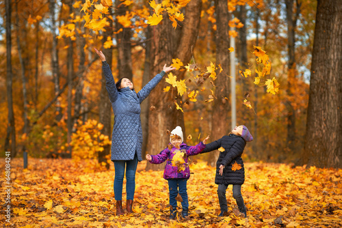 Young mother with two children playes with leaves in the autumn forest photo