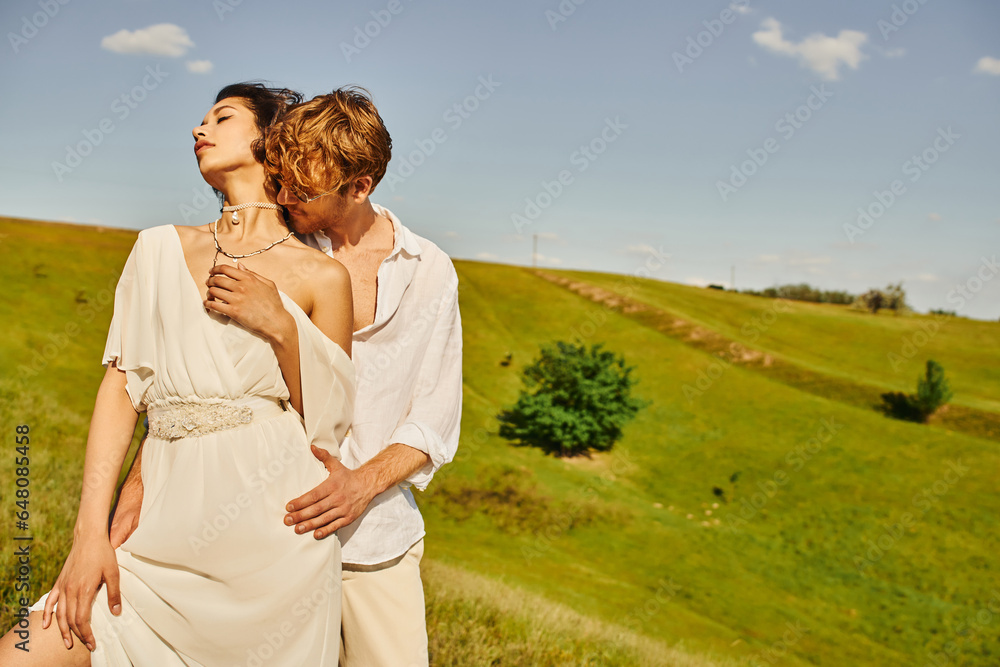 redhead man in sunglasses embracing elegant asian bride on green meadow, tranquil rustic wedding redhead man in sunglasses embracing elegant asian bride on green meadow, tranquil rustic wedding