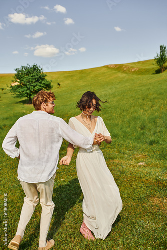 happy newlyweds smiling and dancing in green field, asian bride in wedding dress and redhead groom © LIGHTFIELD STUDIOS