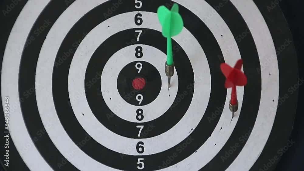 darts fly and stick into a black and white dart board with a red center close-up darts fly and stick into a black and white dart board with a red center close-up