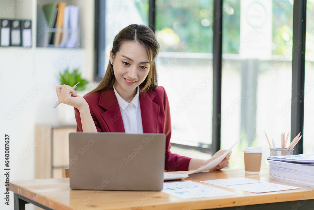 Asian businesswoman working with papers and laptop sitting at table in office, analyzing business accounting calculations and financial planning concepts. Asian businesswoman working with papers and laptop sitting at table in office, analyzing business accounting calculations and financial planning concepts.