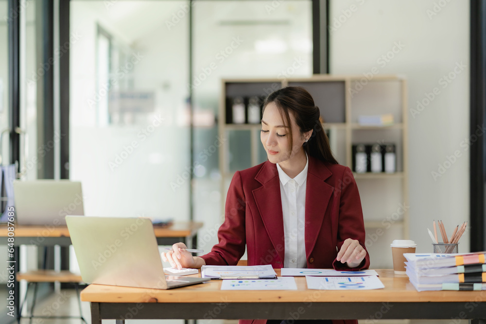 Asian businesswoman working with papers and laptop sitting at table in office, analyzing business accounting calculations and financial planning concepts. Asian businesswoman working with papers and laptop sitting at table in office, analyzing business accounting calculations and financial planning concepts.
