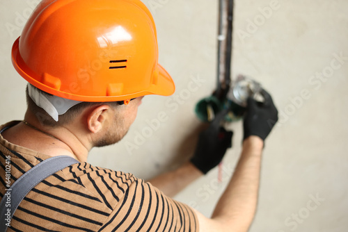 photo electric in uniform, protective gloves and helmet checks presence of electrical voltage in socket phase by electrical tester screwdriver. Examining wires in outlet by voltage detector photo