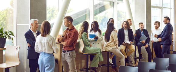 Diverse business professionals communicating at a conference, seminar or other educational event. Young and mature multiethnic people meeting in the office and having discussions. Banner background
