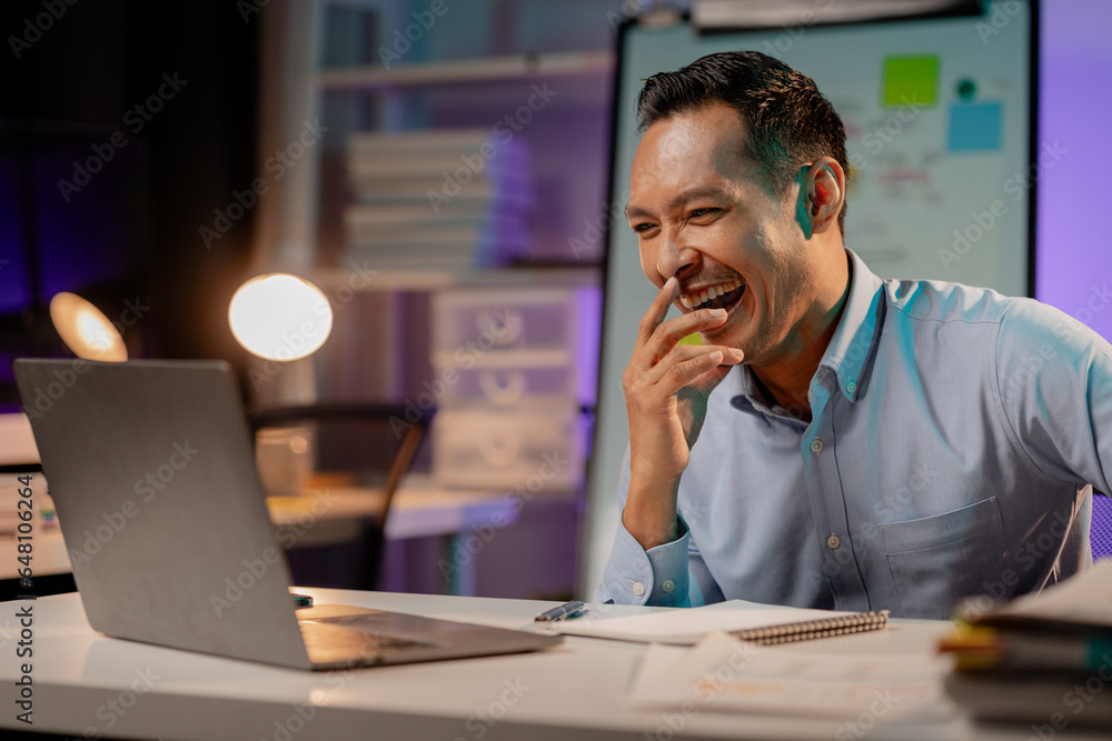 Asian man showing happy expression in the office, company employee working overtime, working late at night, working overtime of a busy and hardworking company employee. Overtime concept. Asian man showing happy expression in the office, company employee working overtime, working late at night, working overtime of a busy and hardworking company employee. Overtime concept.