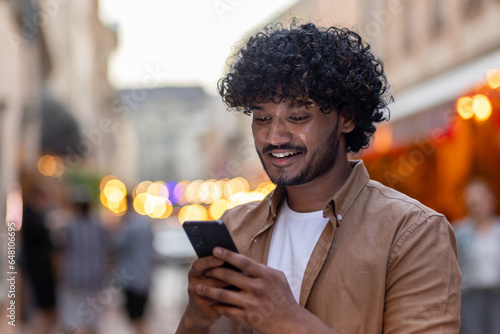 Photography A young Indian man is standing on the street in the city in the evening and using a mobile phone