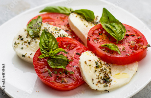 Traditional Italian caprice salad of mozzarella, tomatoes, basil and olive oil, served on a light background.