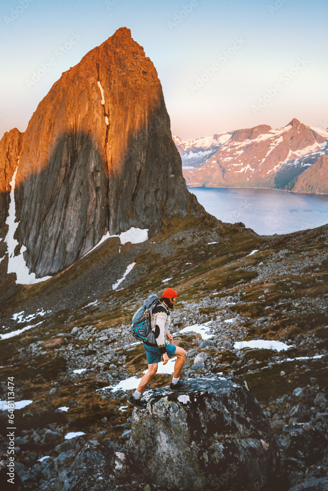 Man hiking alone in Norway mountains travel with backpack outdoor active vacations healthy lifestyle extreme sports exploring Senja island sunset Segla mountain