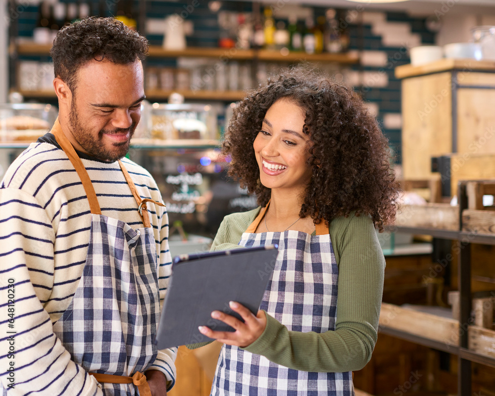 Woman Using Digital Tablet Working In Food Shop Training Man With Down Syndrome Woman Using Digital Tablet Working In Food Shop Training Man With Down Syndrome